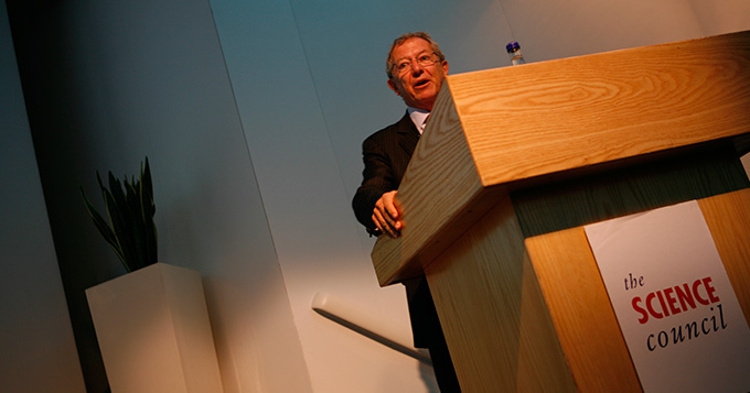 Professor Sir David King standing at a podium delivering a lecture