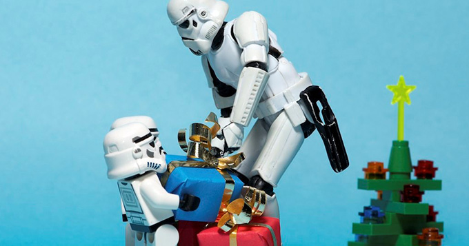 Three Storm Trooper Lego figures are carrying boxes of presents with a Lego Christmas tree in the background