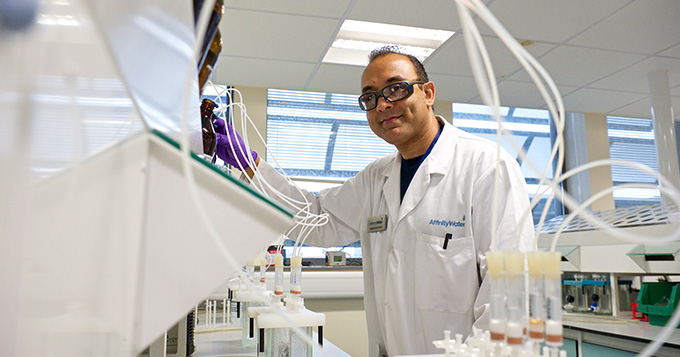 Affinity Water scientist in the lab standing over a bench full of vials and vessels with plastic tubing