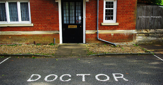 Front door of a doctor's surgery with reserved parking bay in front which has the word 'DOCTOR' written on the ground