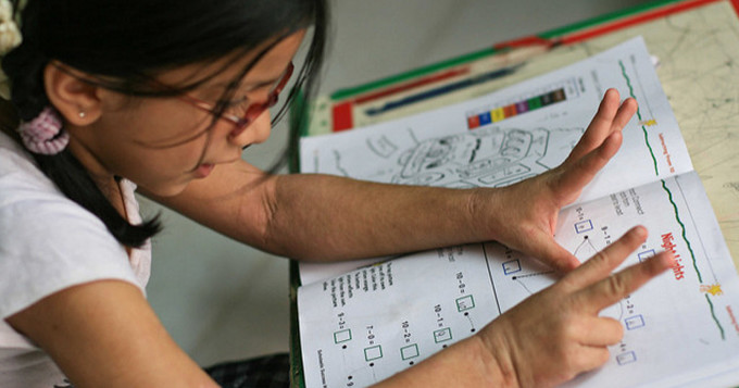 Girl counting numbers with her fingers while studying a maths workbook