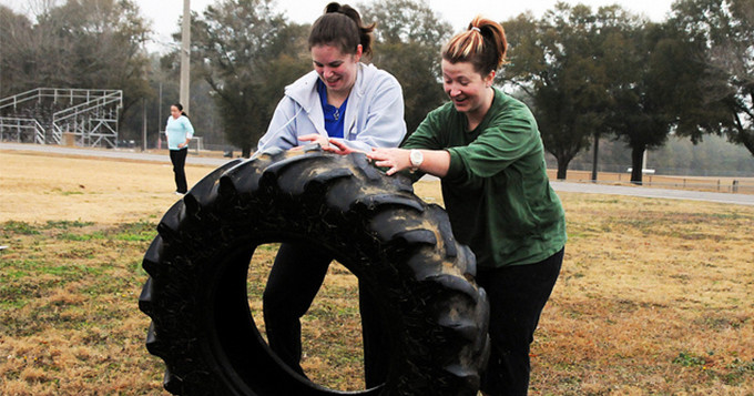 Two women rolling a large tyre as part of fitness bootcamp