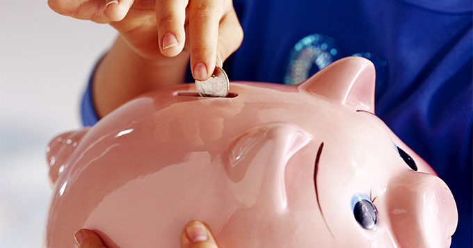 Person inserting a coin into a piggy bank - demonstrating financial assistance