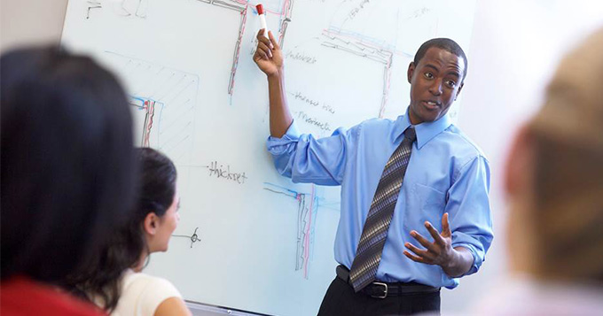 Male teacher standing at a whiteboard teaching a class