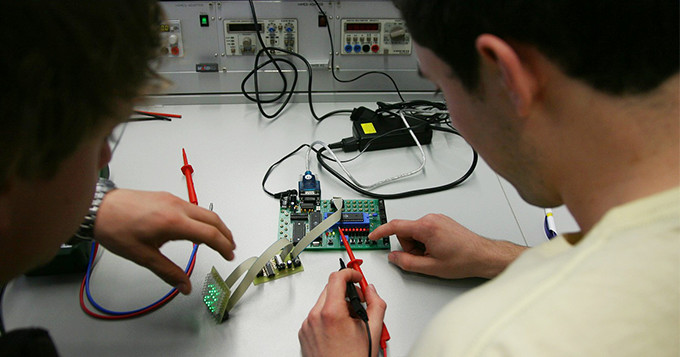 Two technicians working together on a circuit board at a desk