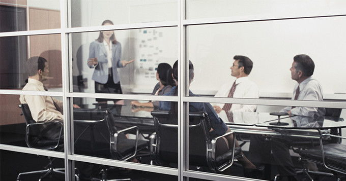 Boardroom meeting with photo taken looking through a glass wall, with male and female colleagues sitting inside