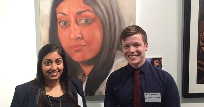 young asian woman and young white man stand in front of painting of the young woman