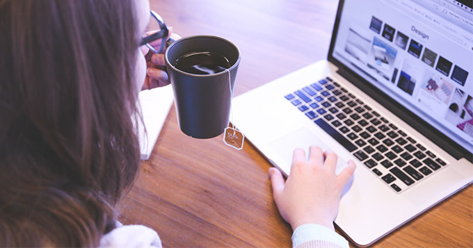 A woman working on a laptop with a mug of tea in one hand