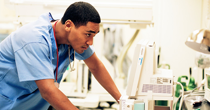 Young male doctor in blue scrubs leans toward computer screen