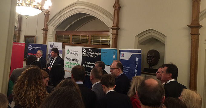 Man standing at podium with banners of various science societies behind him