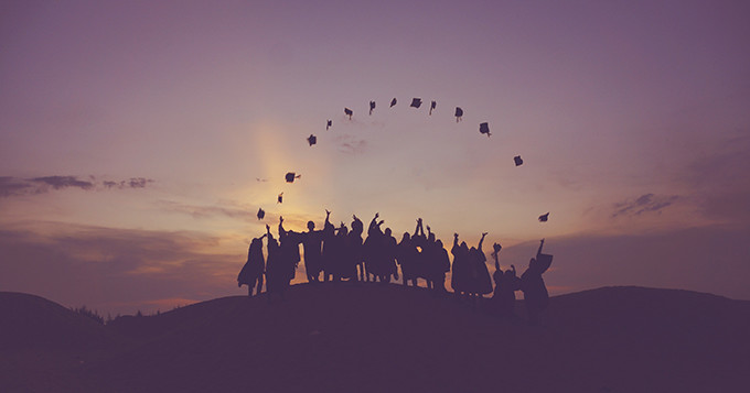 Graduates tossing their hats in the air while standing on a hill at sunset