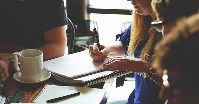 Woman with group of colleagues meeting at a coffee shop and writing in a notebook