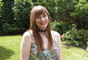 Sharon, Chartered Scientist, stands with a smile in a sunny garden