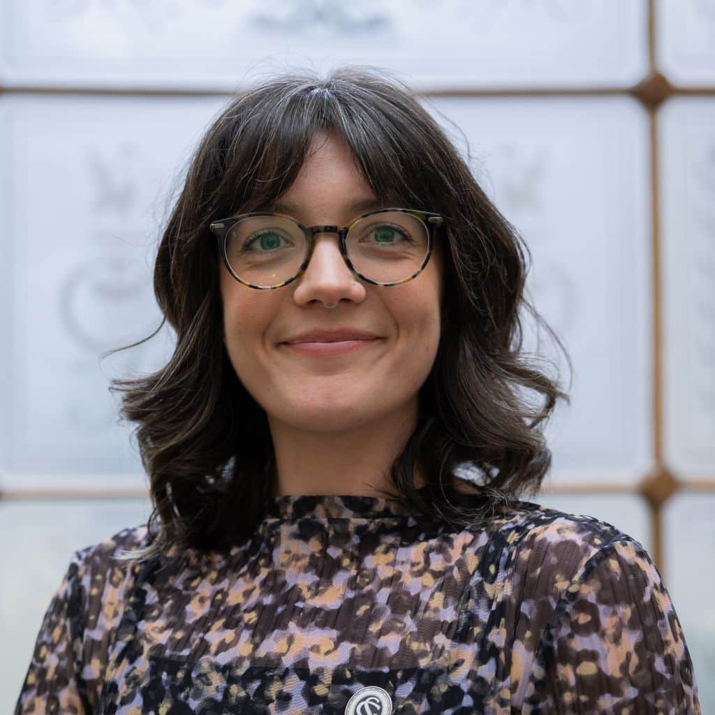 Megan has short, curled brown hair and wears round glasses.
